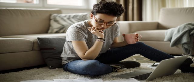 Young woman sat on the floor with pink mug in hand trying to focus on her work