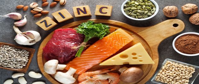 A flatlay of some of the best food sources of zinc on a round wooden serving board against a grey background. Zinc food sources of animal origin products such as meat, fish, cheese and eggs are laid out alongside vegan and plant-based sources such as pump