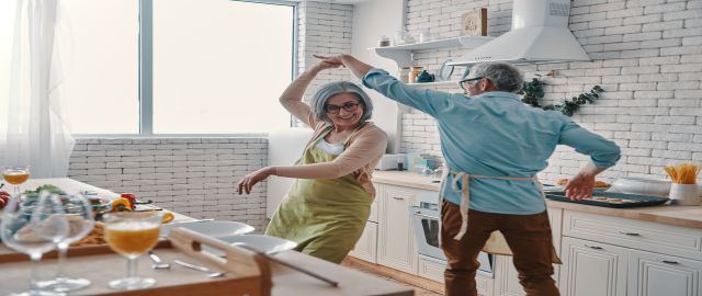 Image of happy senior man and woman dancing in their kitchen for blog on sarcopenia