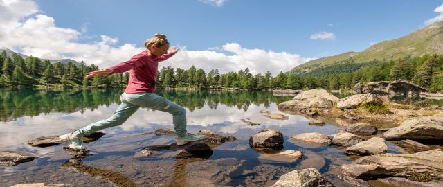 Female hiker stepping across rocks running through a lake