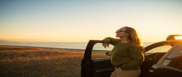 Mid-life woman enjoying sunset over the sea on the beach near her car. She looks relaxed and has perimenopause rage under control.