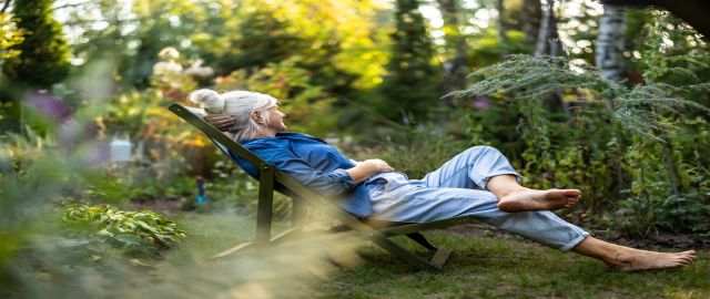 Mature woman relaxing in a deckchair in a shaded area of her garden.