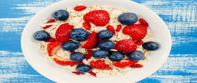 Bowl of porridge topped with strawberries and blueberries, on a blue background