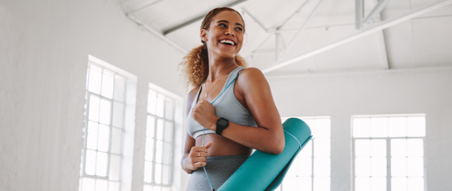 Gut microbiome and the gut brain axis blog image of a young healthy woman wearing gym leggings and sports top holding a yoga mat.