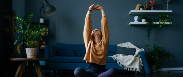 A women sat cross-legged on the floor in front of a sofa stretching.