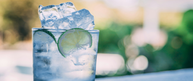 Close up of a tumbler of water filled with ice and a slice of cucumber.