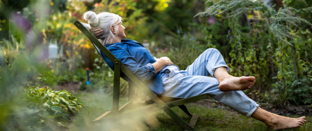 Mature woman relaxing in a deckchair in a shaded area of her garden.