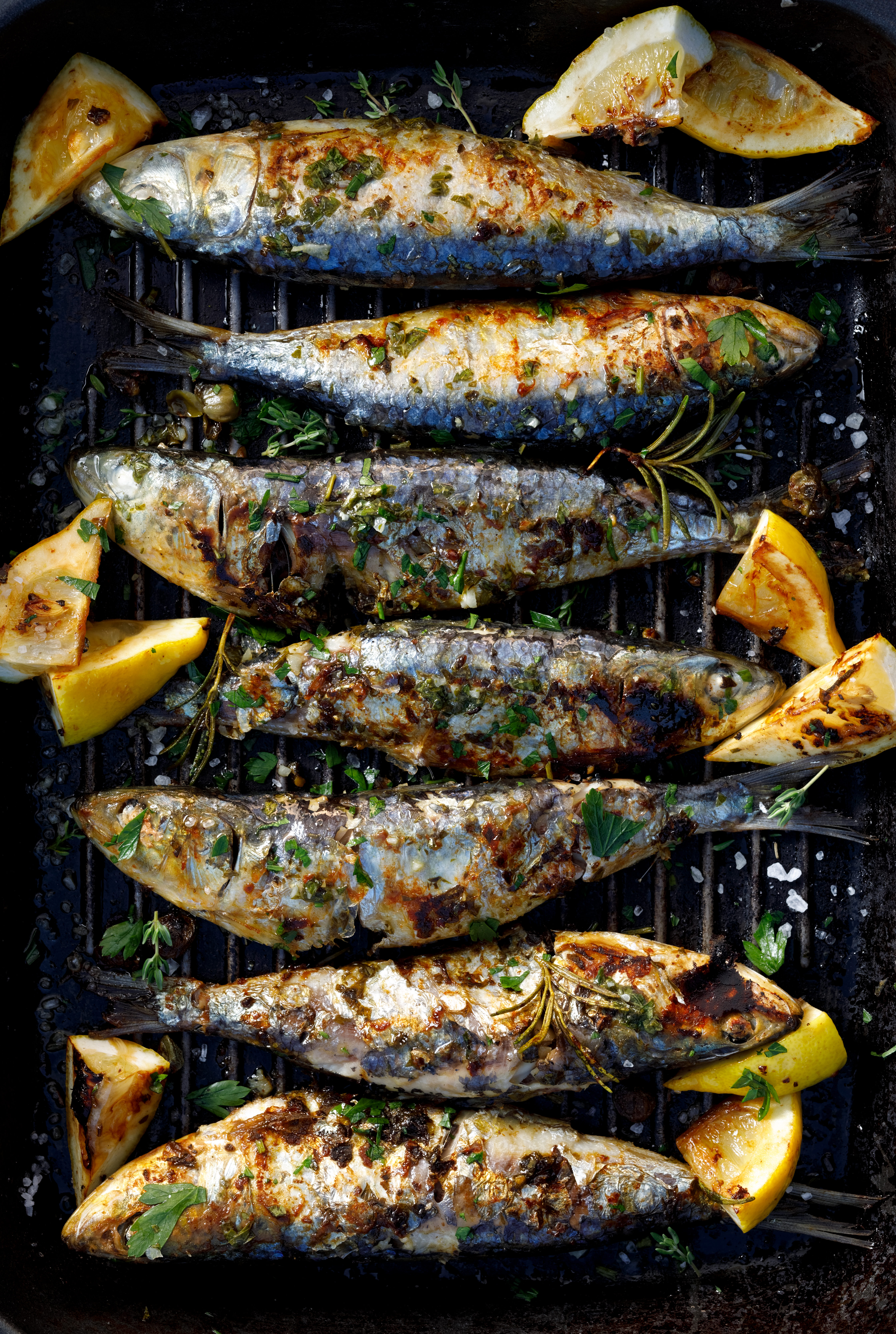 Top view of chargrilled whole sardines and lemon quarters on a grill plate. Sardines are considered part of a heart healthy diet.