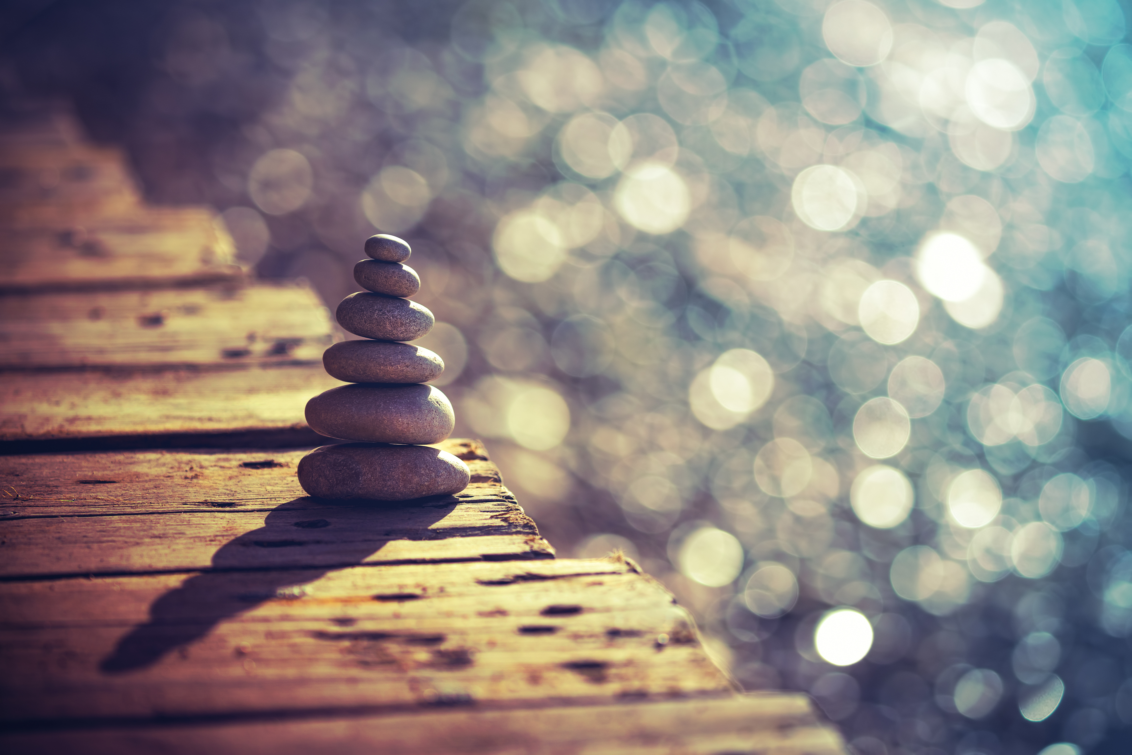 A pile of pebbles on the wooden bridge on the beach. Conveying balance, stillness and calm - feelings and qualities that practising mindfulness can also help you to access.