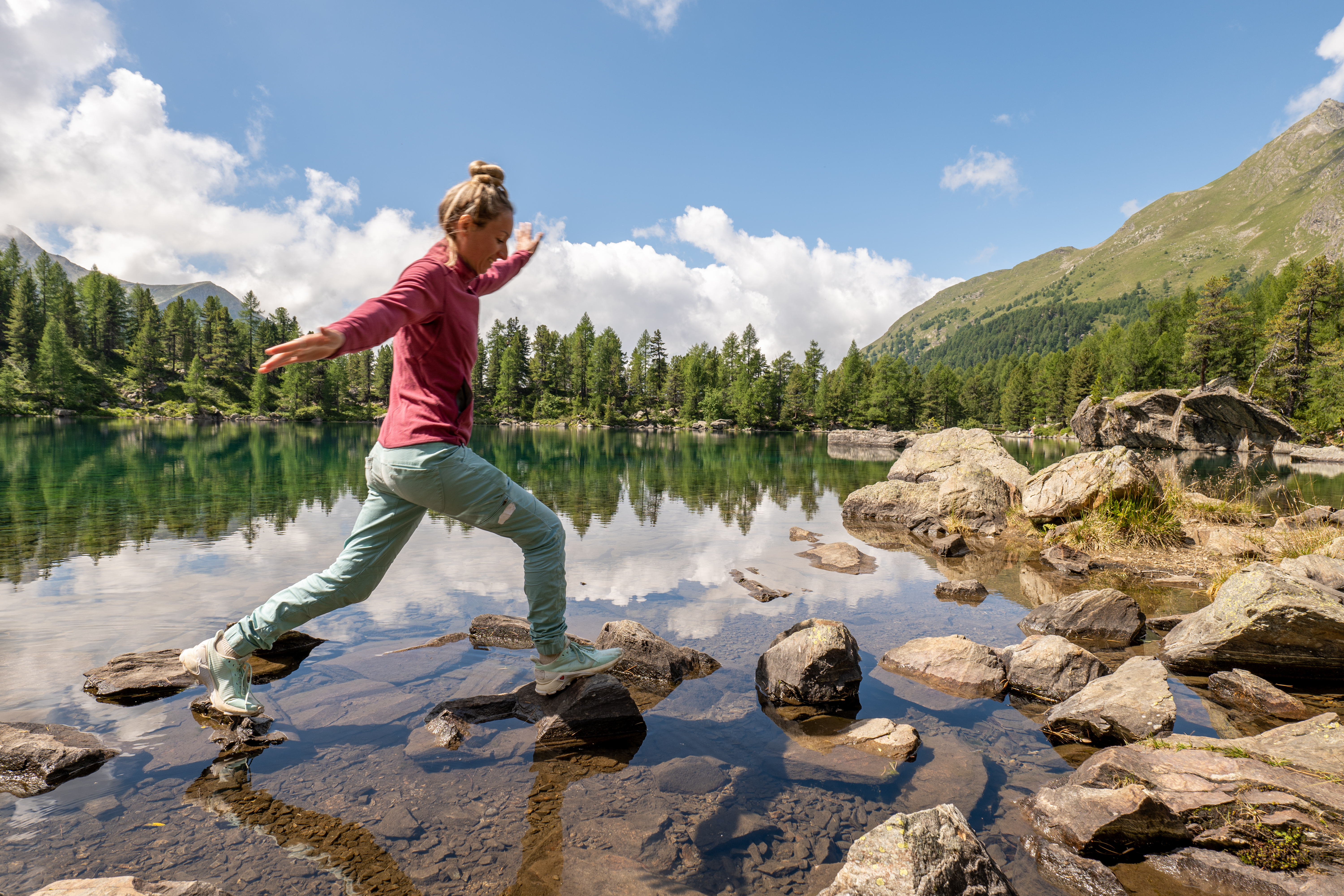 Female hiker stepping across rocks running through a lake