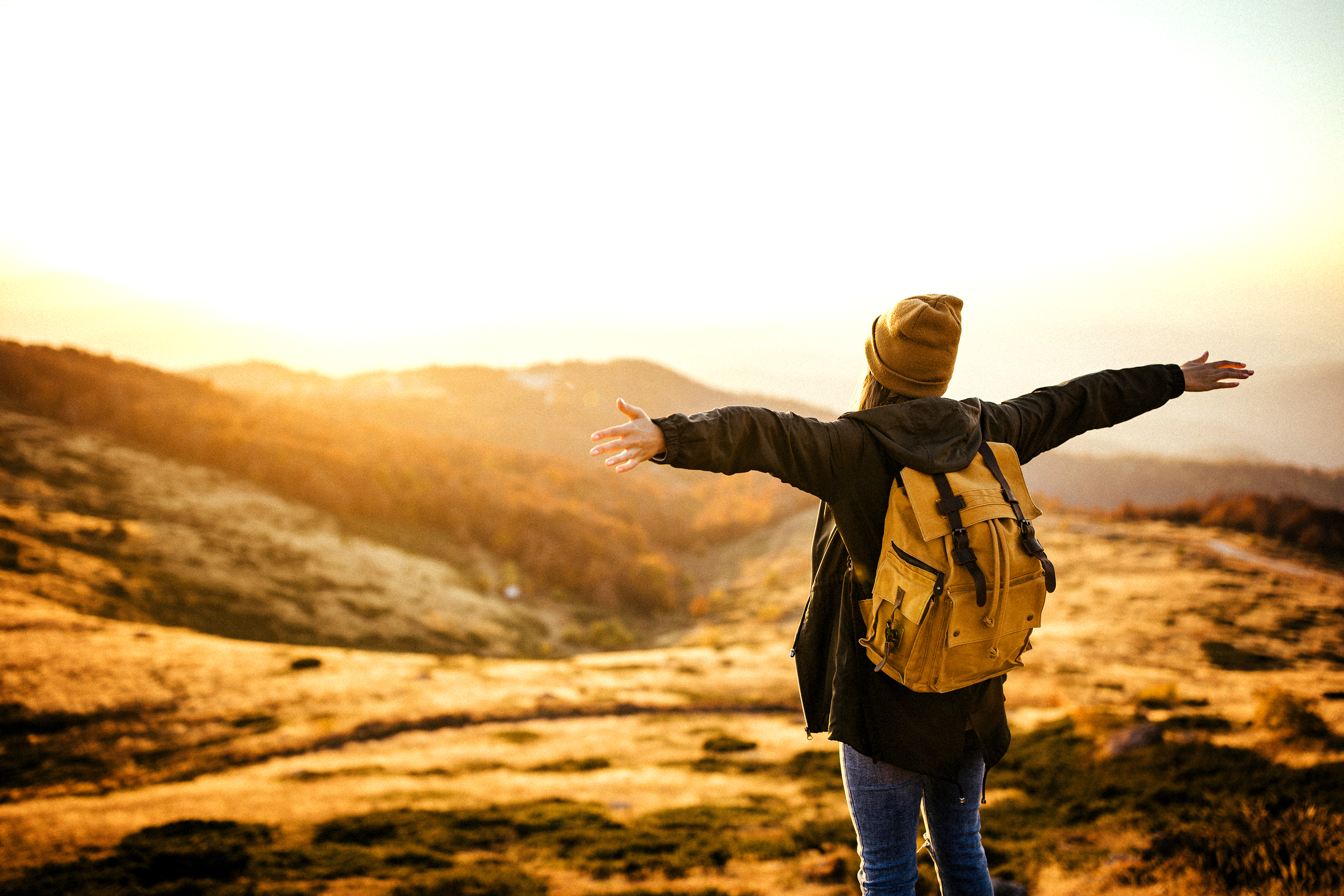 Rear view of hipster woman feeling full of energy on the top of the hill with outstretched arms looking at view