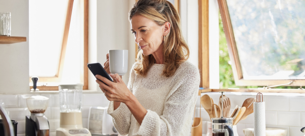 Stylish 50 something woman in her kitchen holding a mug and phone researching whether antioxidants can help the immune system.